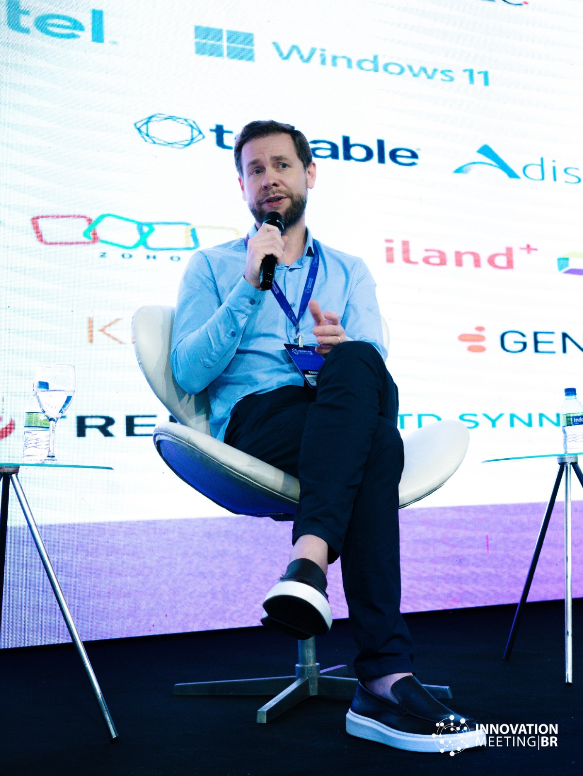 Everton Dzikovicz sentado no palco, de microfone, durante um painel no Innovation Meeting Brasil.